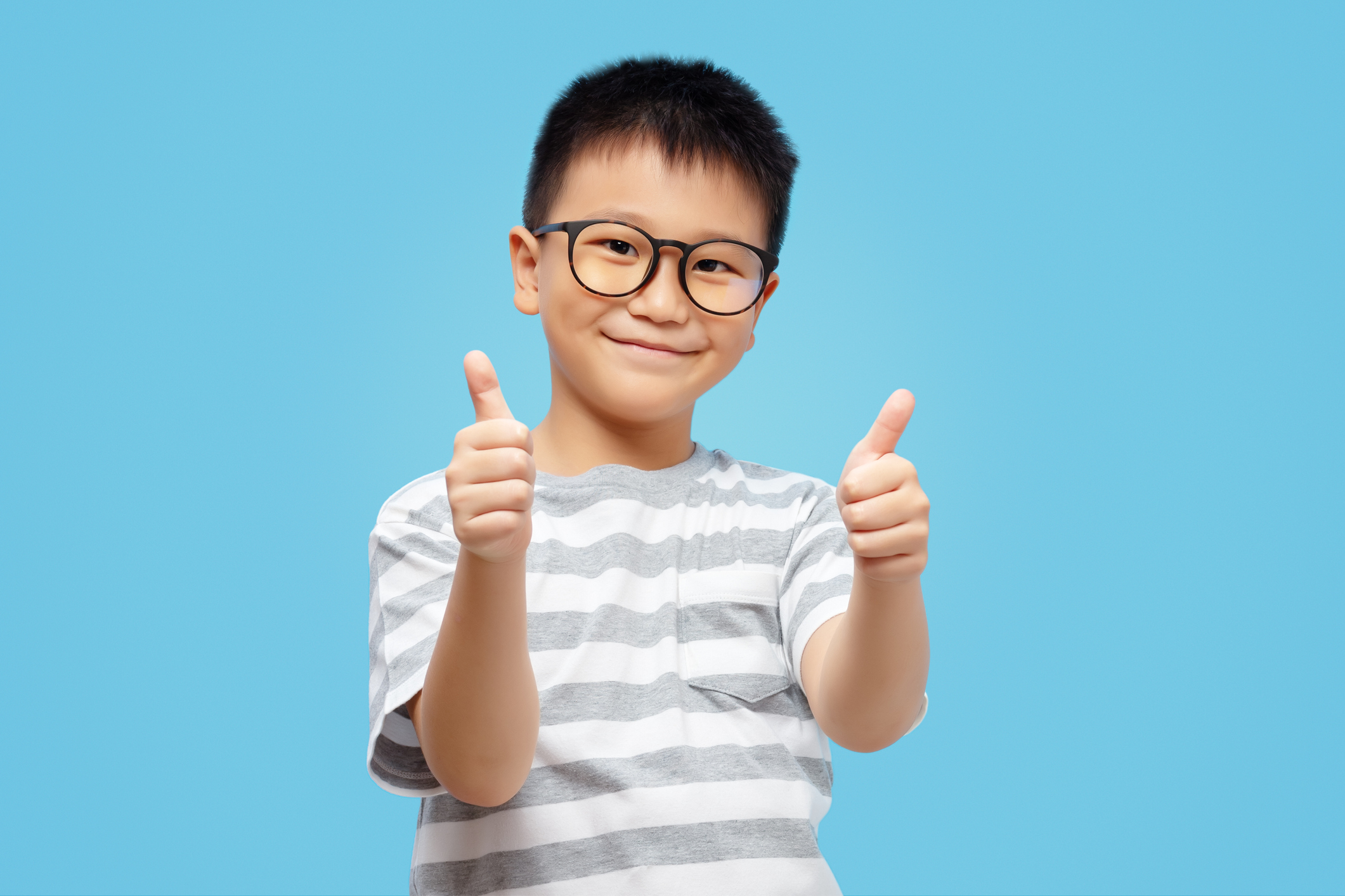 Happy kid showing thumbs up, wearing eyeglasses on blue background